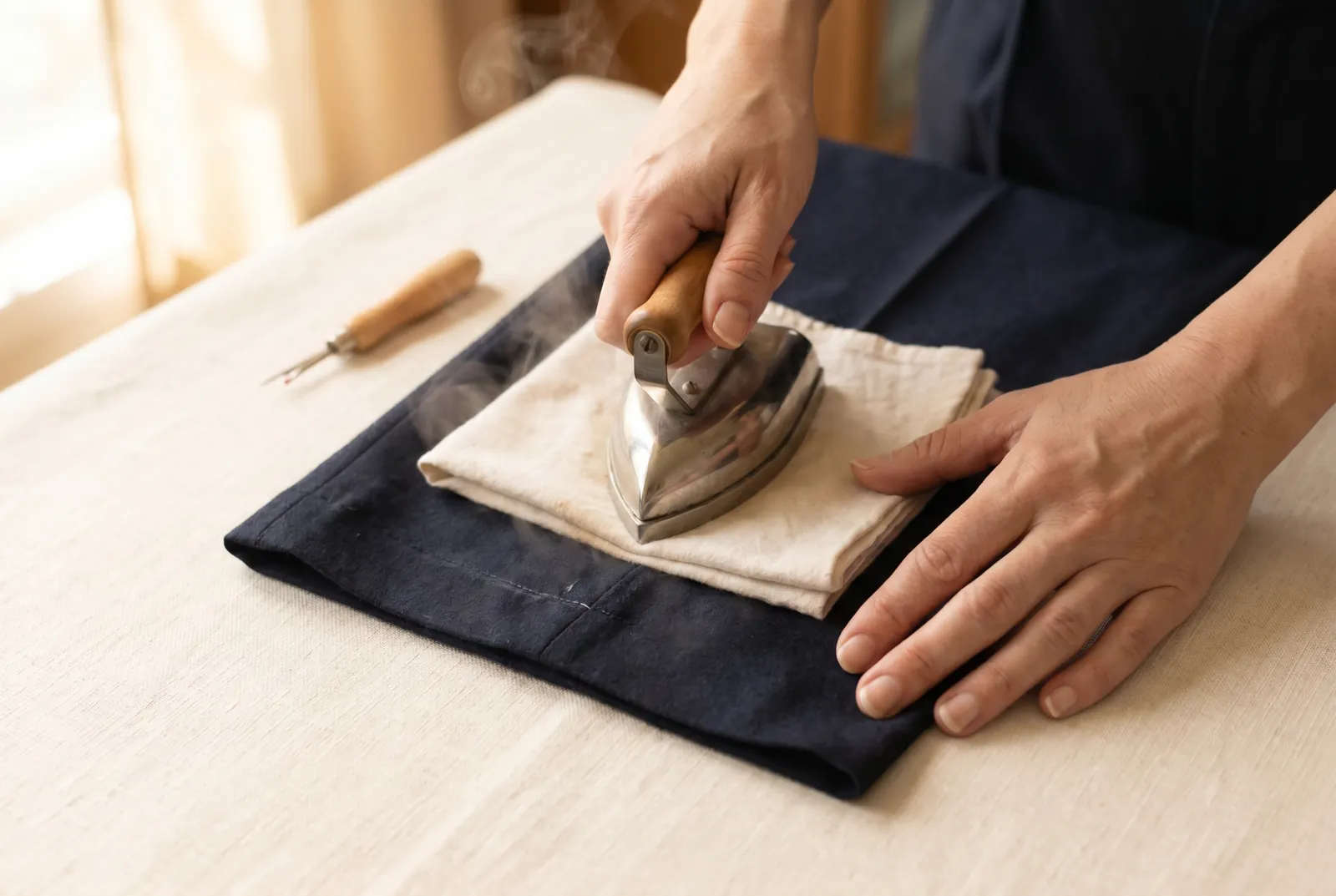 Photo: Lay the opened hem flat on the wrong side, cover it with the damp cloth, and press with a hot iron until the old fold line disappears.