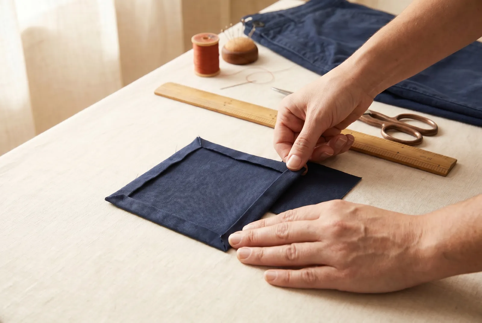 Photo: Turn each of the four edges of the patch 6 mm (1/4 in) over toward its right side, and crease each fold along a thread.